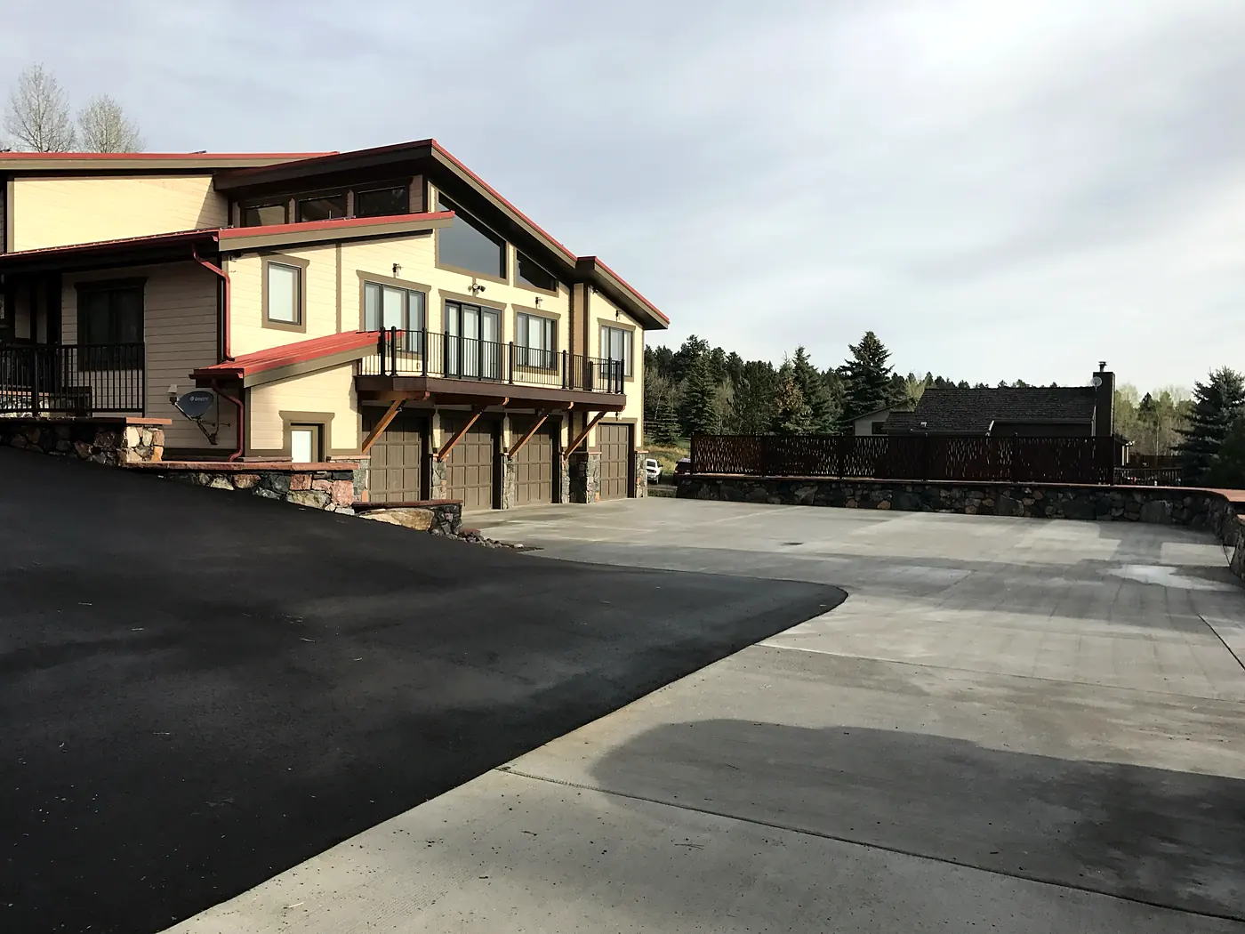 Asphalt driveway transitioning to a large concrete parking court beside a mountain home in Evergreen, Colorado