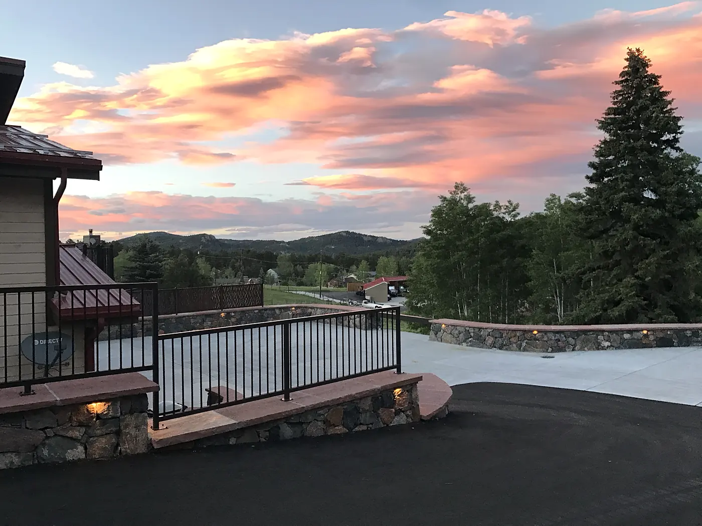 Asphalt driveway meeting a concrete parking court with lit stone walls at sunset, Evergreen, Colorado