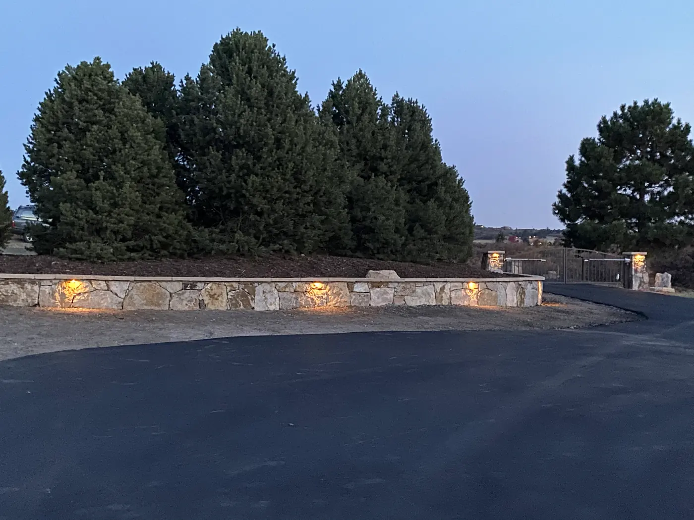 Asphalt driveway beside a low stone wall with built-in lights at dusk, Salida, Colorado