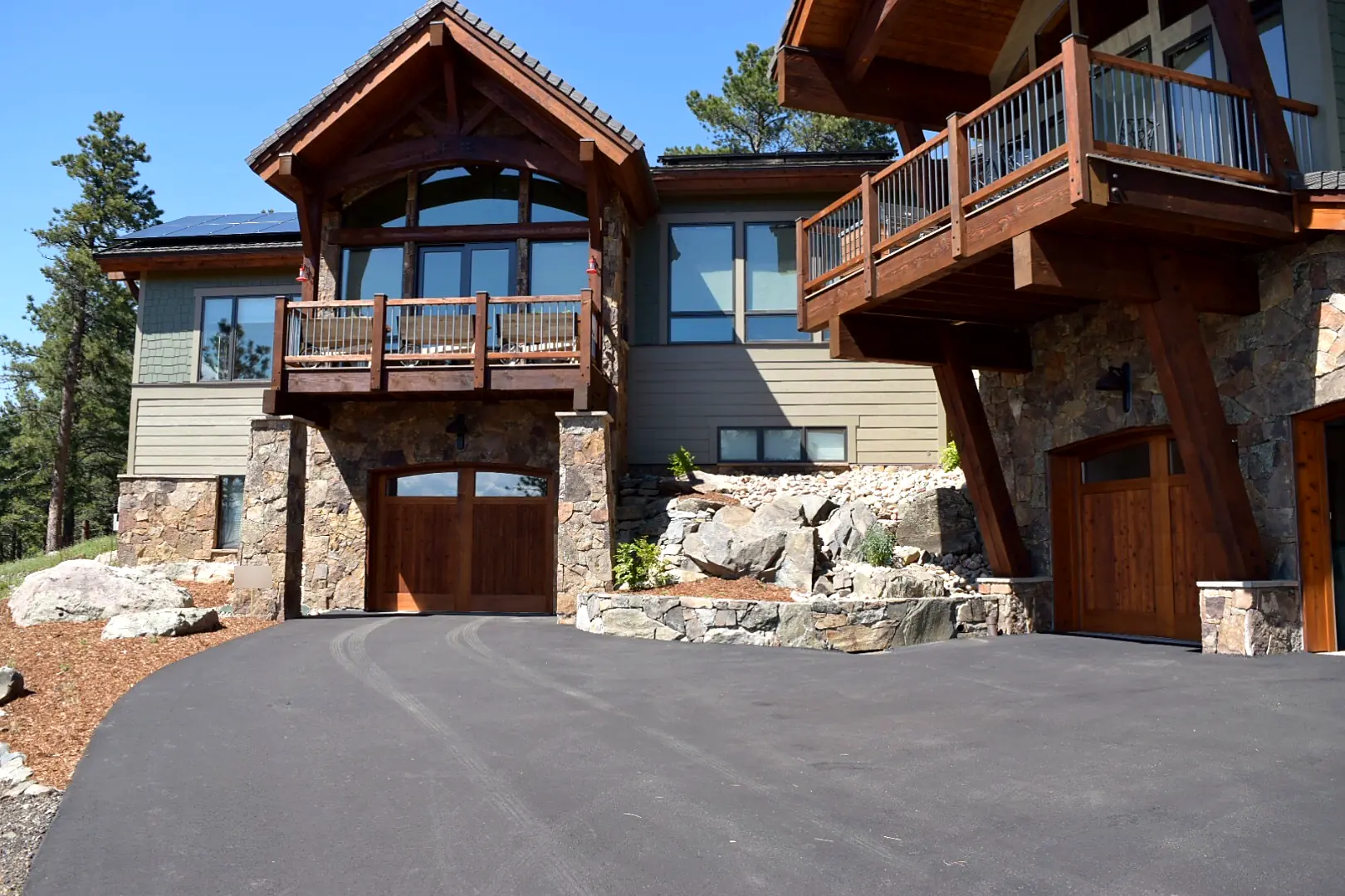 Asphalt driveway in front of a timber-frame mountain home with boulders and a stone wall, Genesee, Colorado
