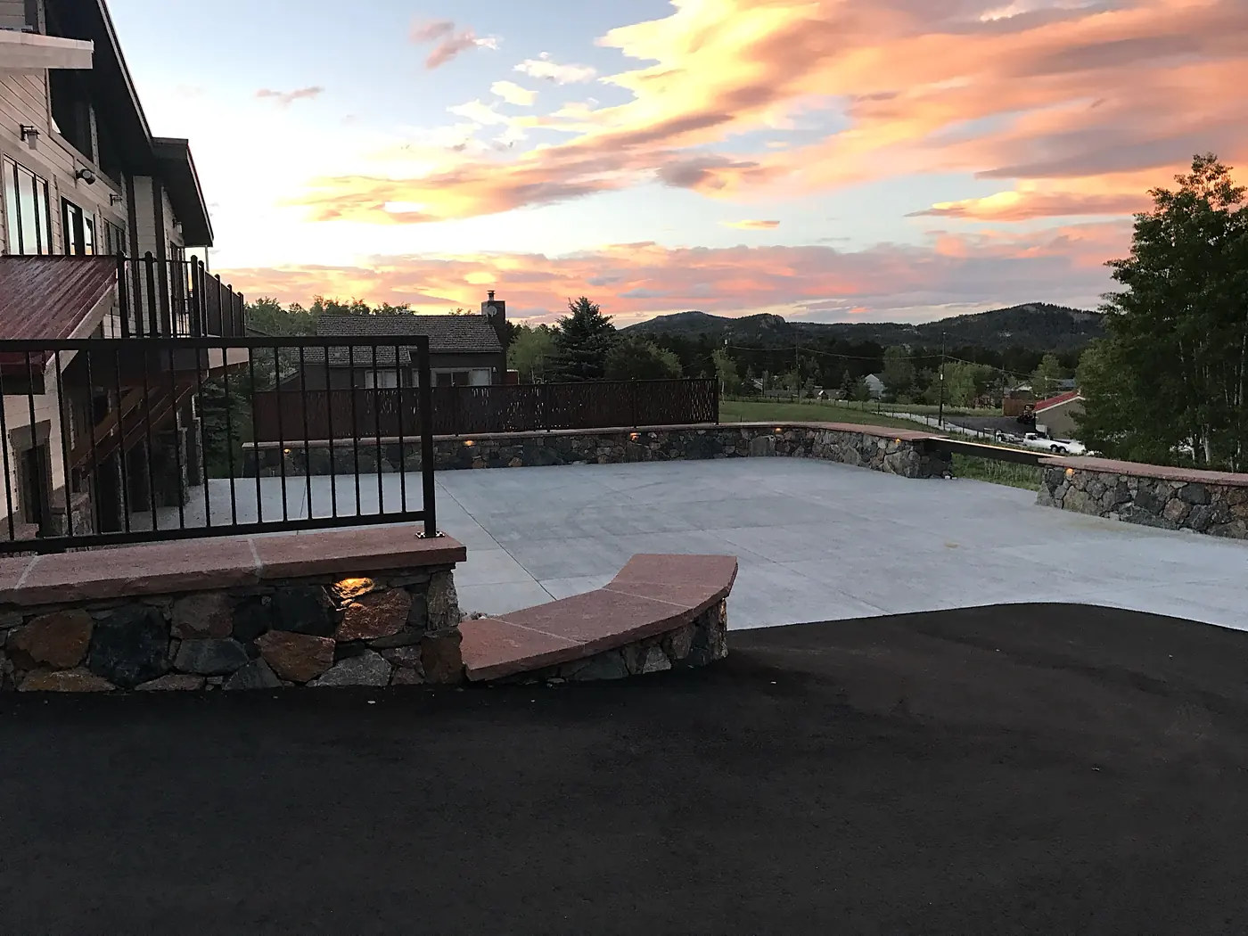Concrete parking court edged with lit stone walls at sunset, Evergreen, Colorado